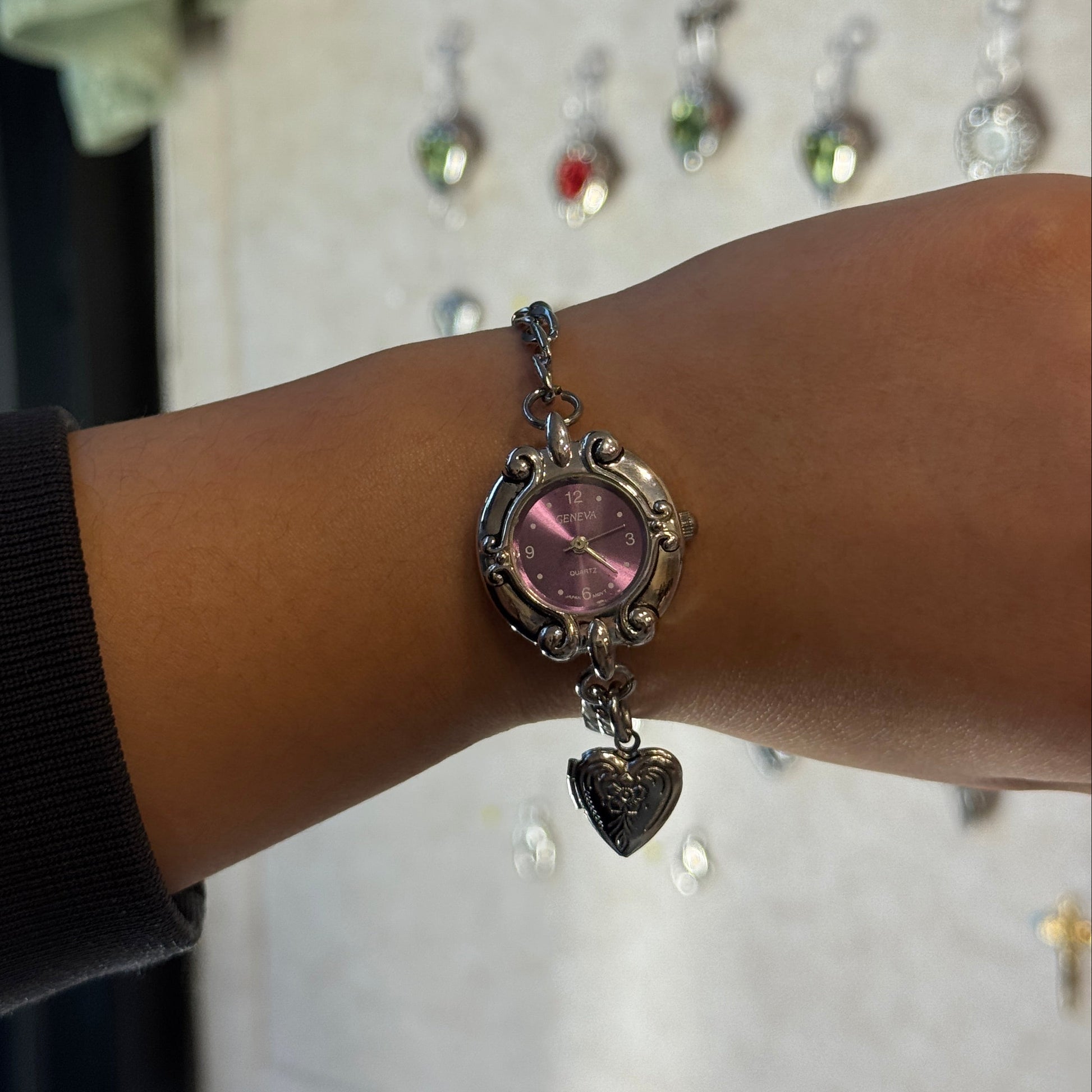 Watch bracelet with a purple gemstone on a wrist, blurred background with jewelry display.