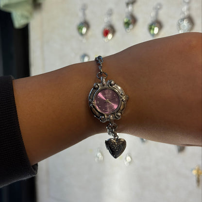 Watch bracelet with a purple gemstone on a wrist, blurred background with jewelry display.